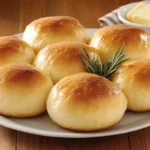 Plate of golden brown no-yeast dinner rolls garnished with a sprig of rosemary and served with a butter dish on the side.