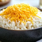 Shredded cheese on rice in a bowl with a spoon.